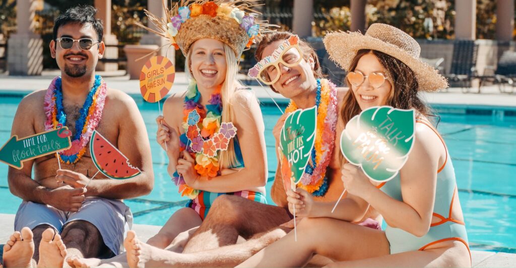 group sitting by pool in swimsuit hold funny photo props