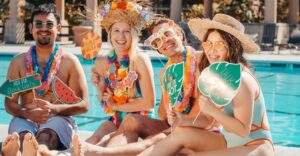 group sitting by pool in swimsuit hold funny photo props