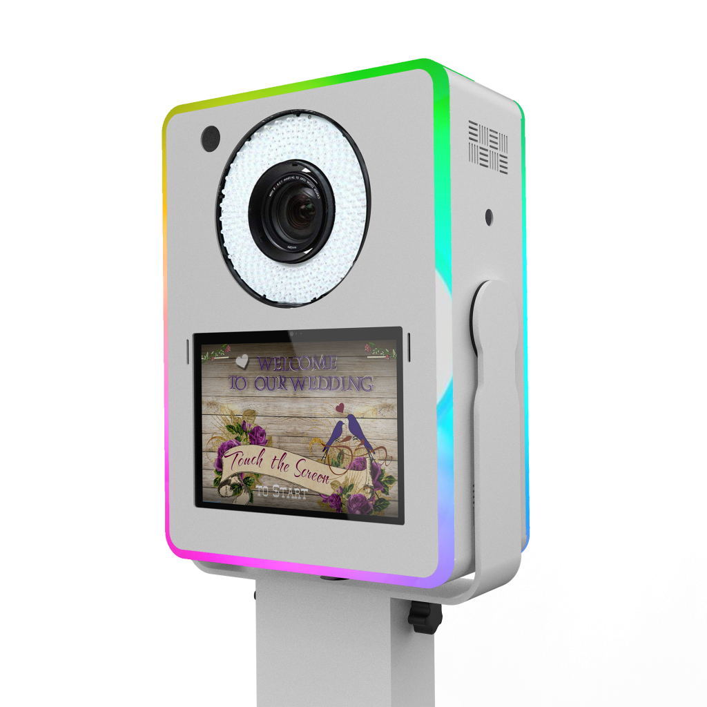 A 3/4 perspective view of a white Lumia M photo booth head unit with glowing RGB chasing LED edges, showing the integrated ring light and a touch screen displaying a wedding-themed welcome graphic.